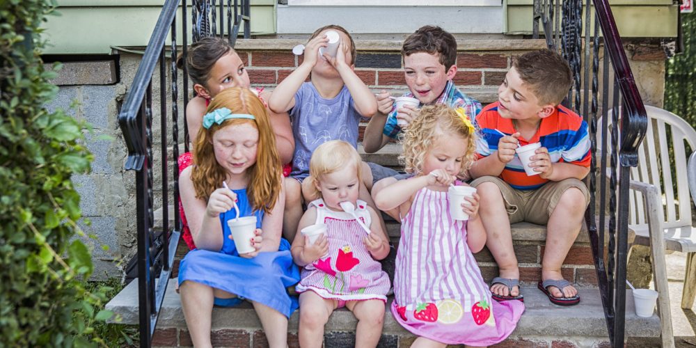 Seven children sitting on doorstep eating ice cream